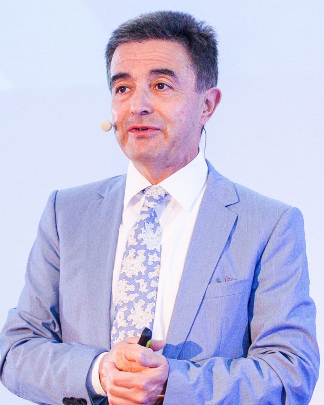 Prof. Dr. Fouad Khoury spricht mit Ansteckmikrofon auf einer Bühne, im hellgrauen Sakko mit gemusterter Krawatte.