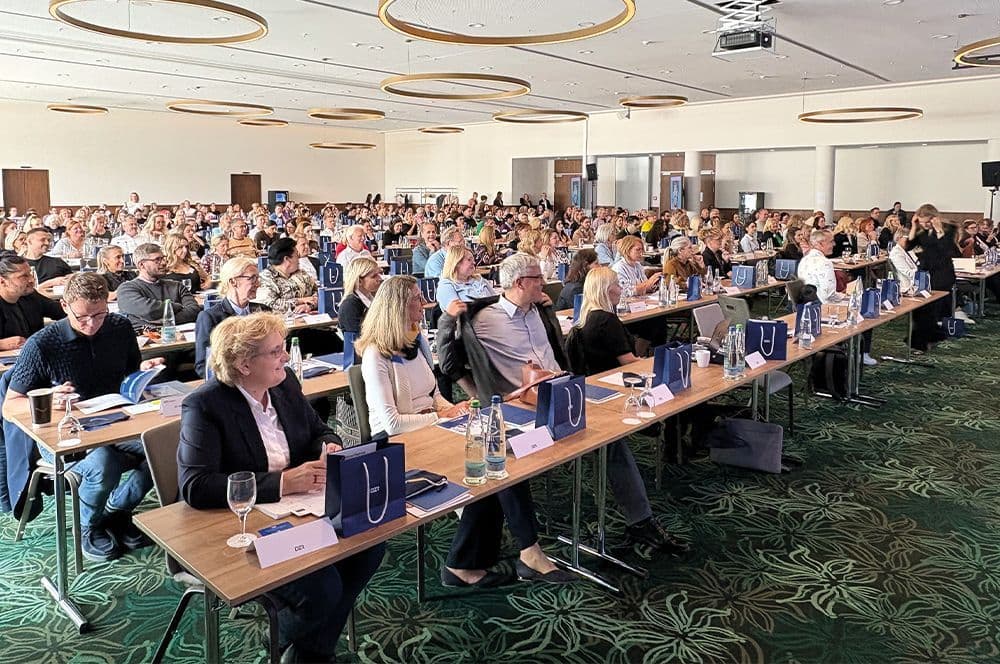 Großer Konferenzsaal mit Teilnehmern an langen Tischen und blauen DZR-Kongresstaschen