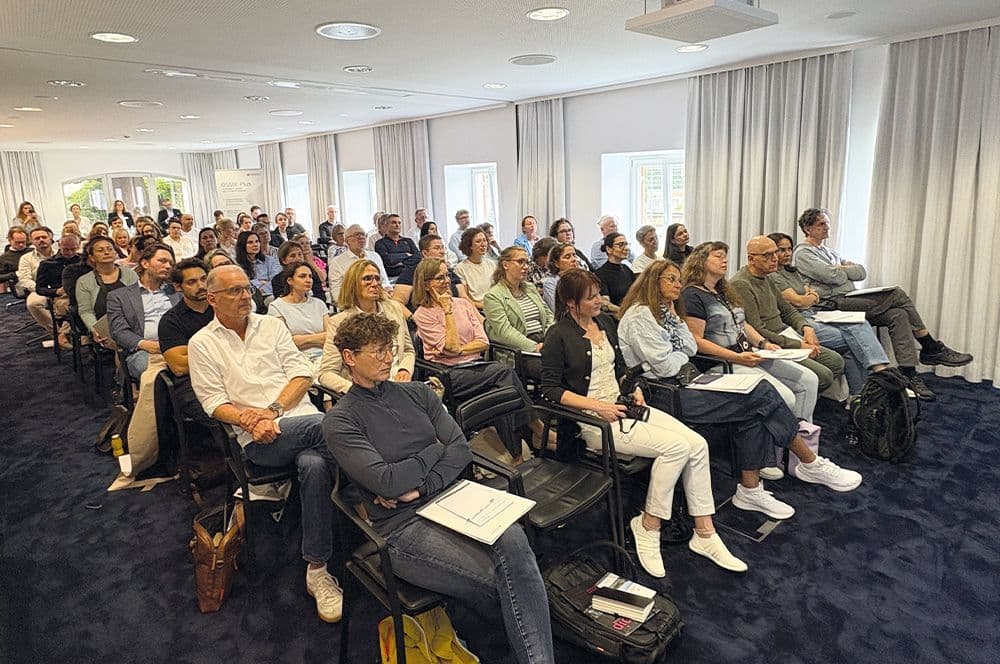Teilnehmende sitzen in hellem Seminarraum mit Vorhängen bei einer Präsentation